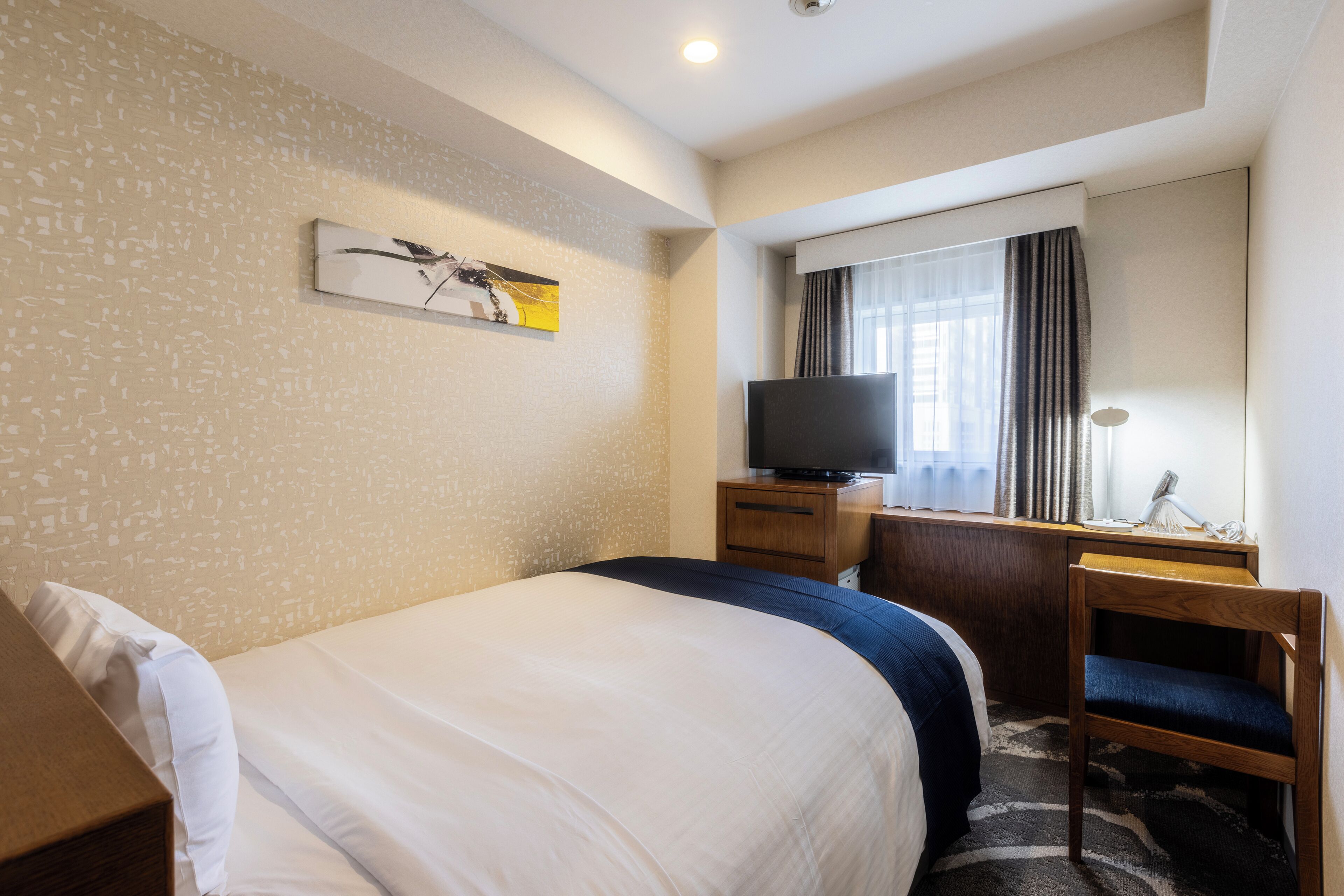 Habitación de hotel con cama, escritorio con televisor, silla y ventana con cortinas.