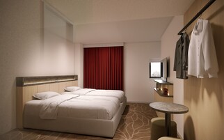 A hotel room with a bed, a small round table, a mirror, and a red curtain.