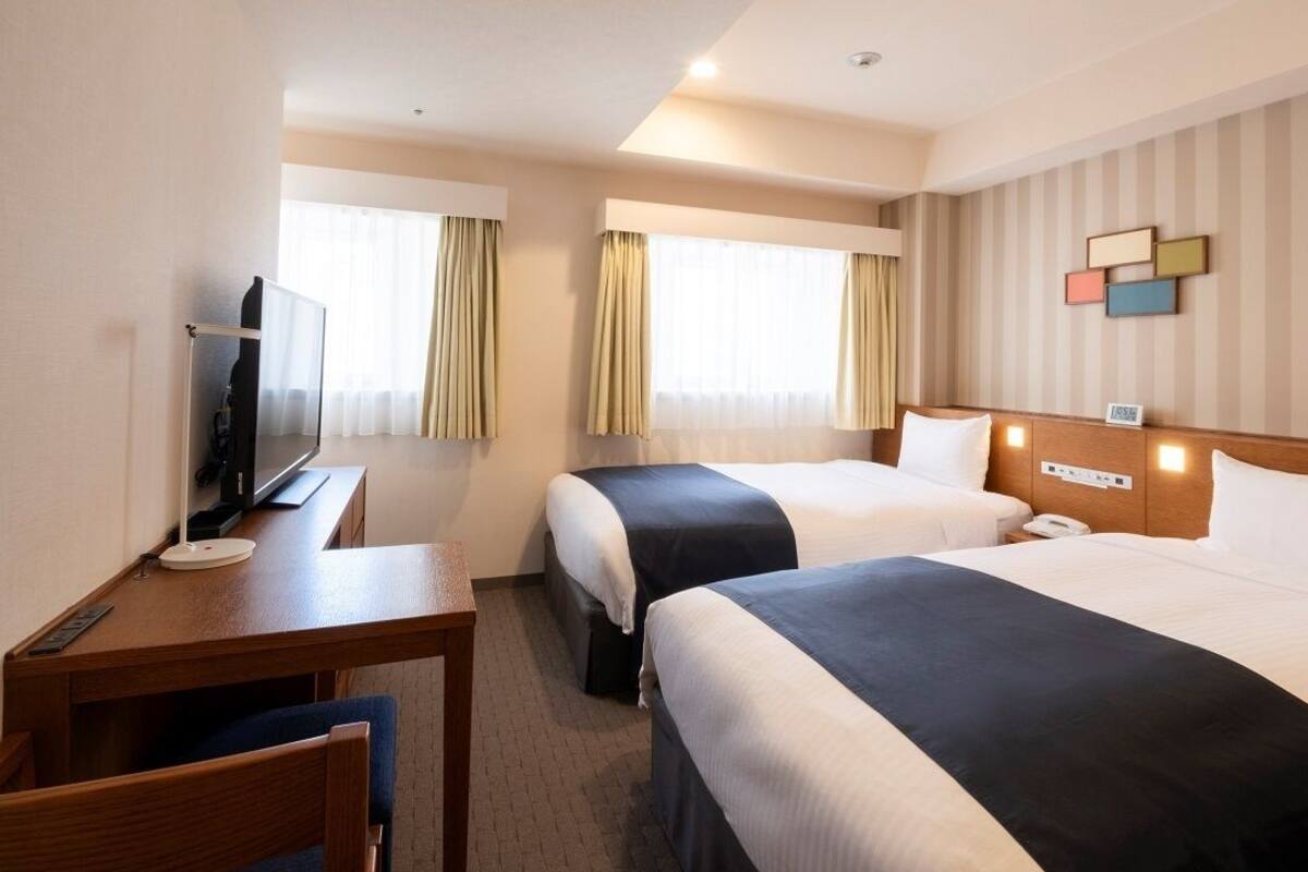 A hotel room with two beds, a desk, a TV, and a wall-mounted phone.