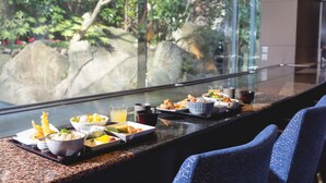 A dining table with various dishes and drinks, set against a backdrop of a glass window overlooking a garden with rocks and greenery. - Shinjuku Washington Hotel Main (Tokyo)