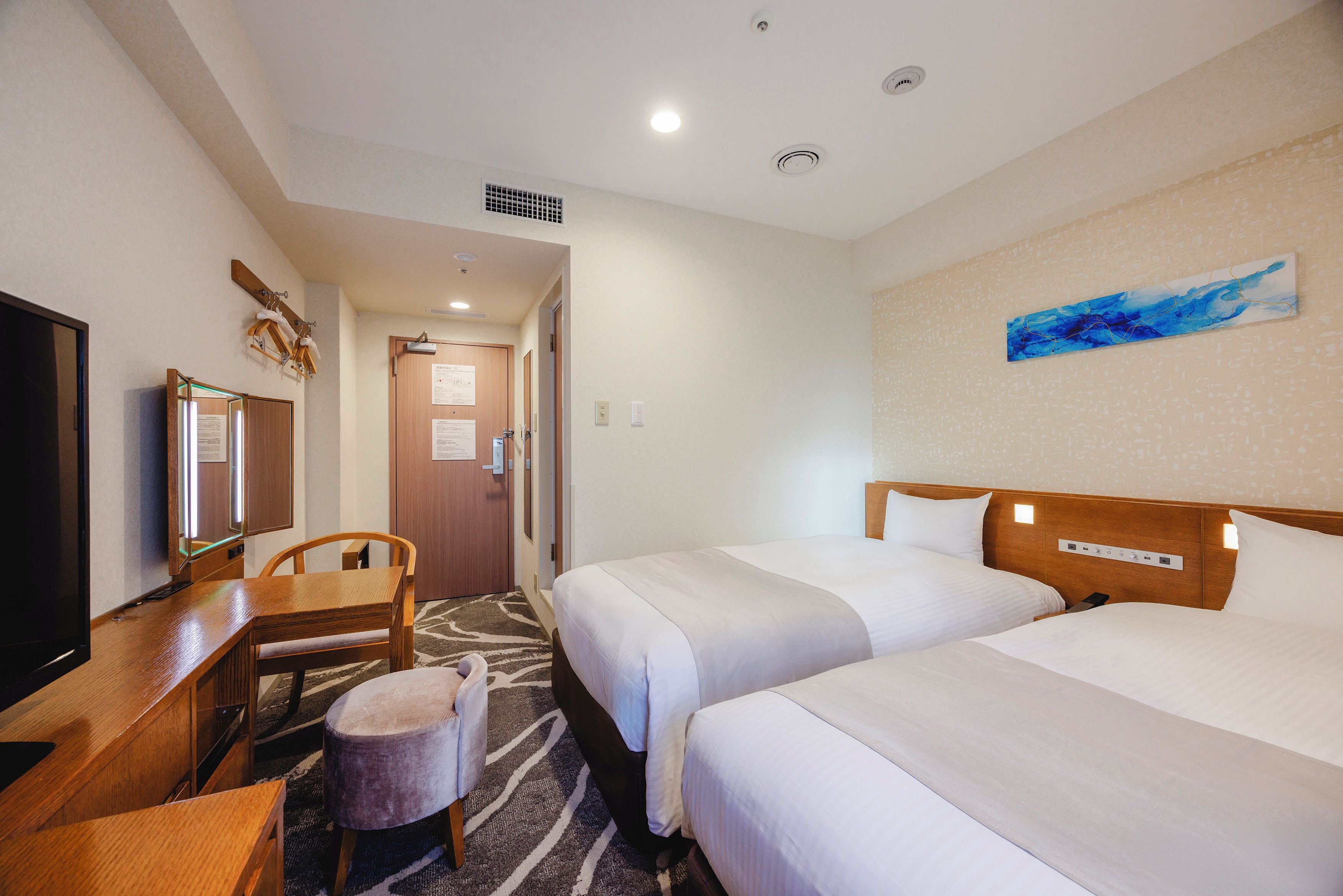 A hotel room with two beds, a desk with a chair, a television, and a painting on the wall.
