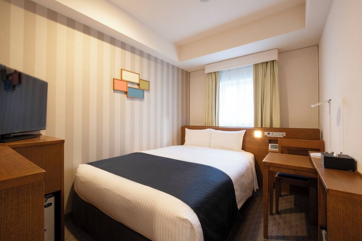 A hotel room with a large bed, a desk, a television, and a window with curtains.