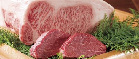 A large piece of raw meat with a wooden cutting board and green herbs.