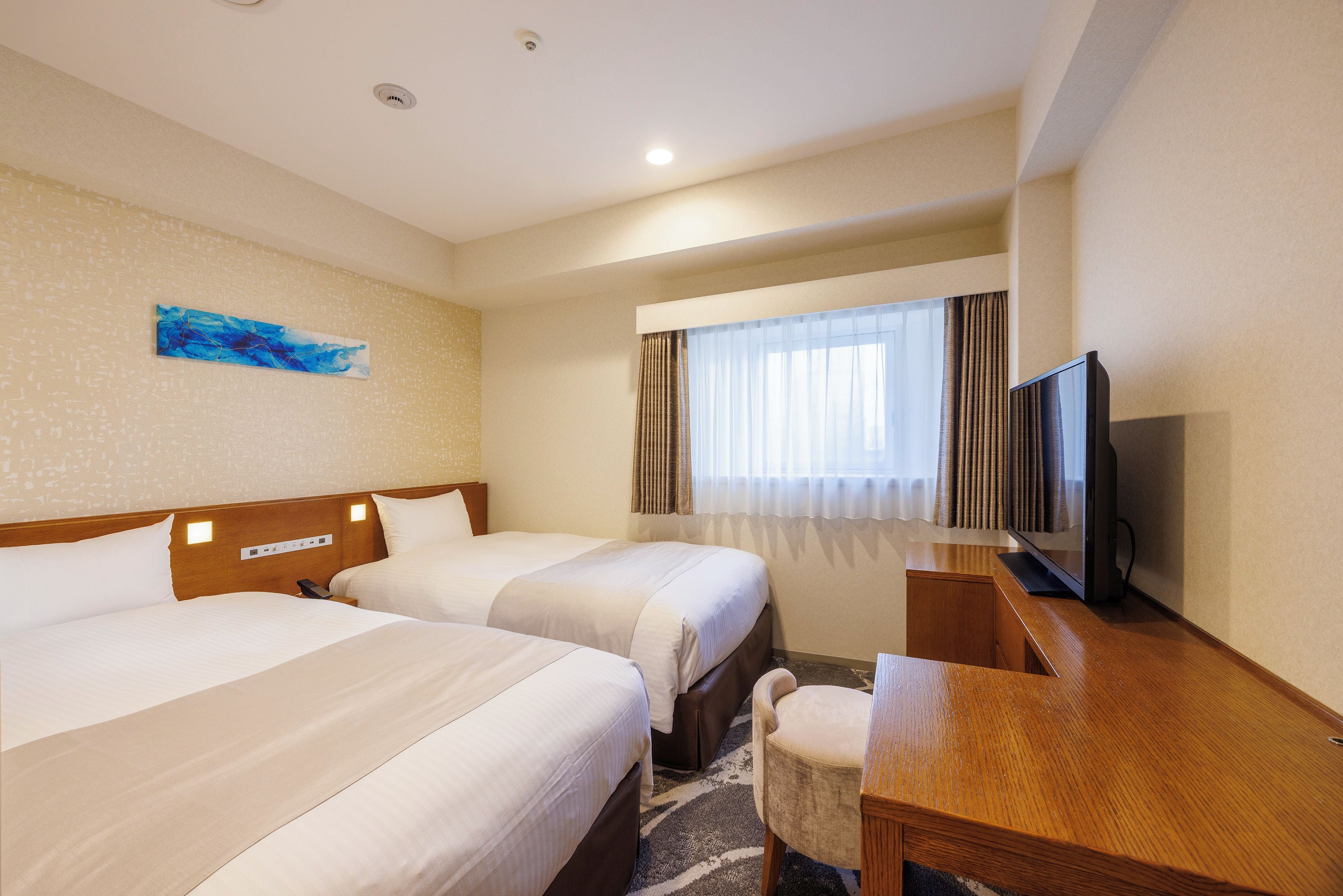 Habitación de hotel con dos camas, televisión, escritorio y ventana con cortinas.