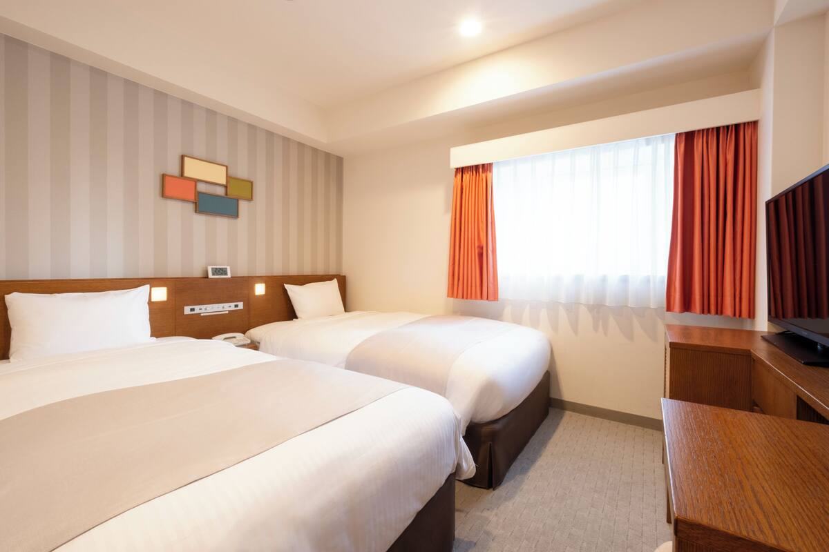 A hotel room with two beds, a wooden headboard, a desk, and a television.