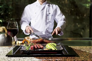Un chef preparando comida en una parrilla, con una copa de vino tinto y un plato de verduras cortadas.