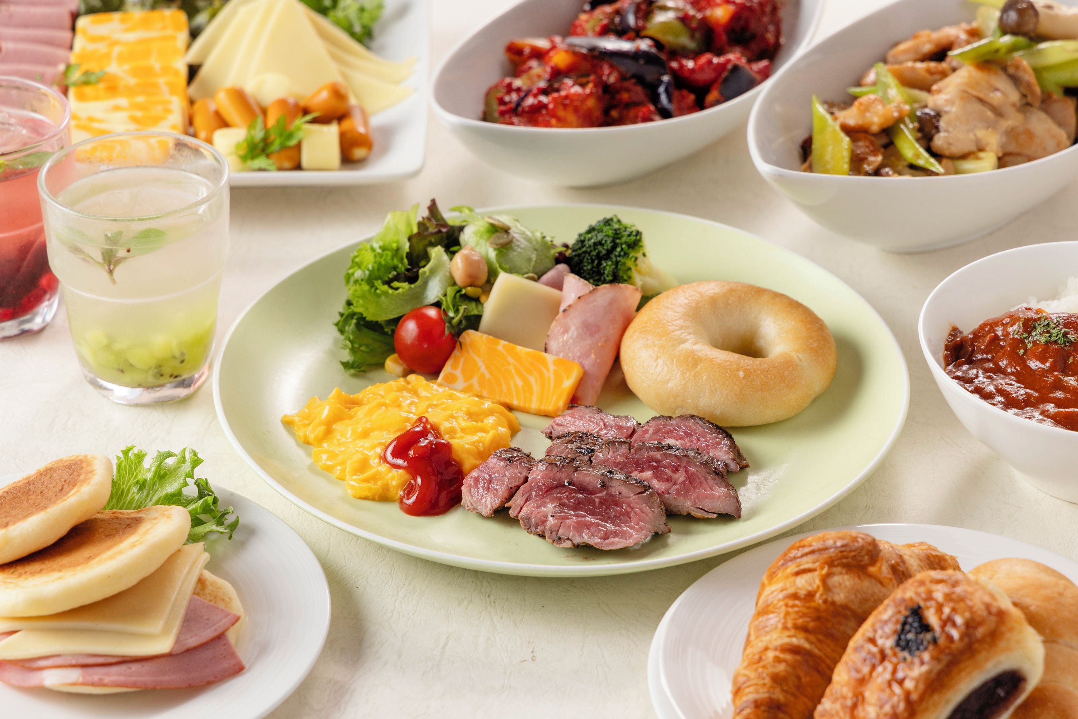 A variety of food items on a table, including a plate with eggs, ham, and vegetables, a glass of beverage, and several other dishes.