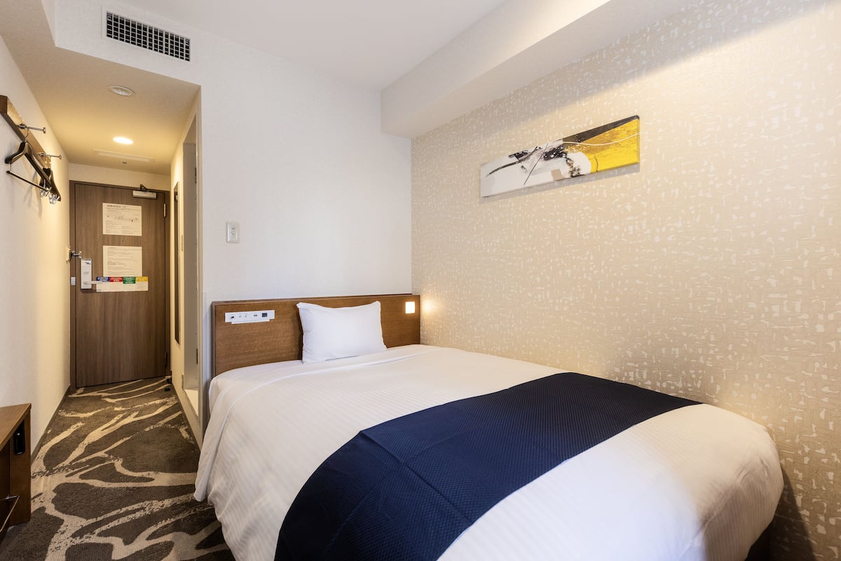 A hotel room with a bed, a headboard, a wall-mounted artwork, and a carpeted floor.