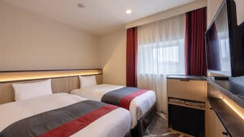 Habitación de hotel con dos camas, un escritorio, un televisor y una ventana con cortinas.