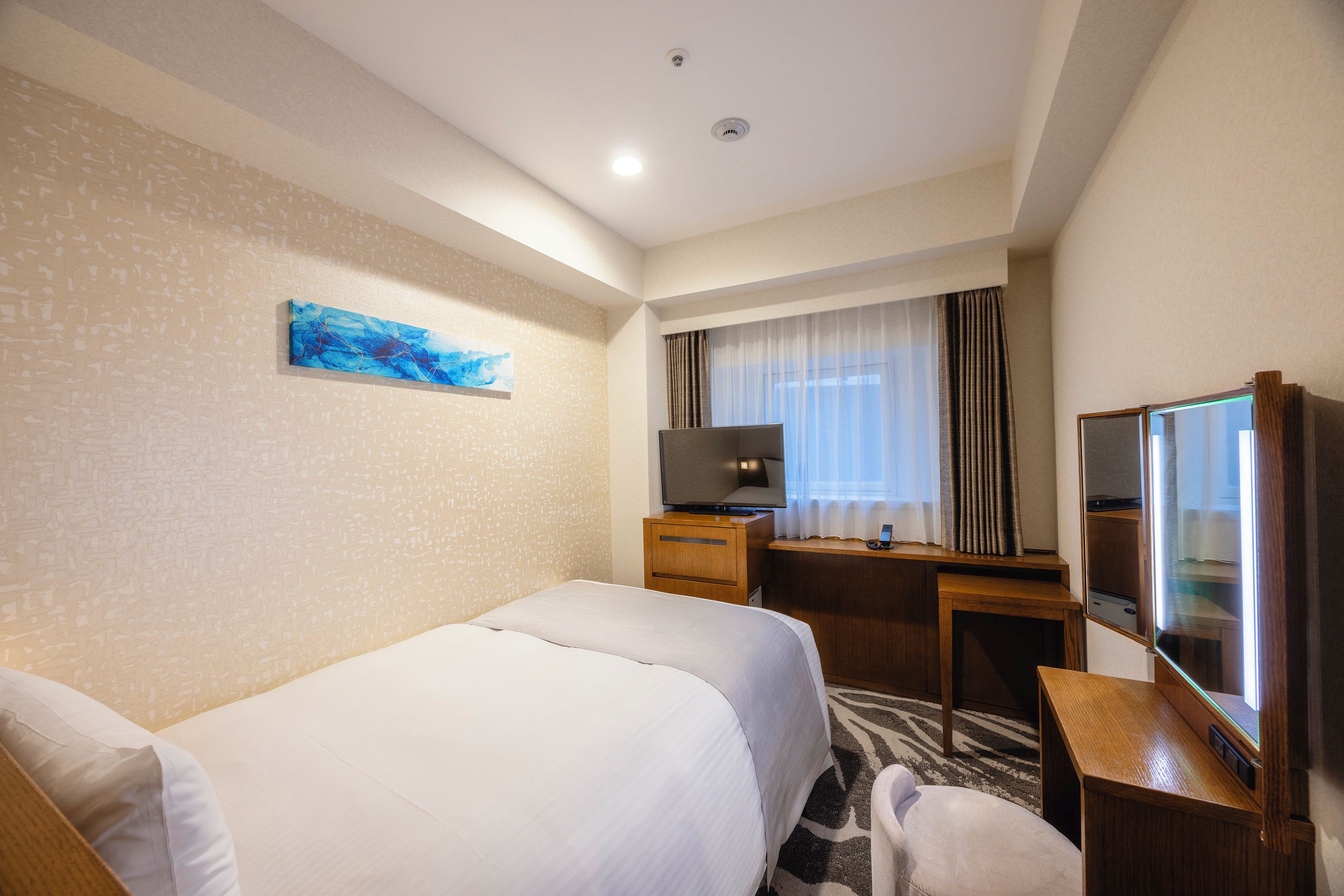 A hotel room with a bed, a desk, a television, and a mirror.