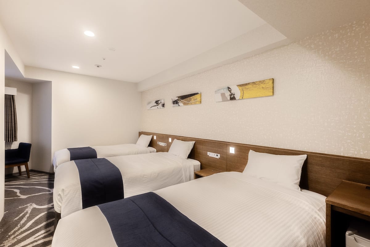 A hotel room with three beds, a wooden headboard, a small bedside table, and a wall-mounted artwork.
