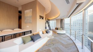 A modern hotel room with a curved seating area, a large window with a city view, and a staircase leading to an upper level.