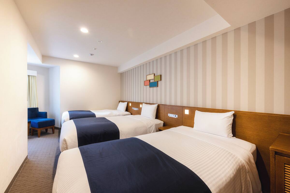 A hotel room with three beds, a wooden headboard, a striped wall, and a small table.