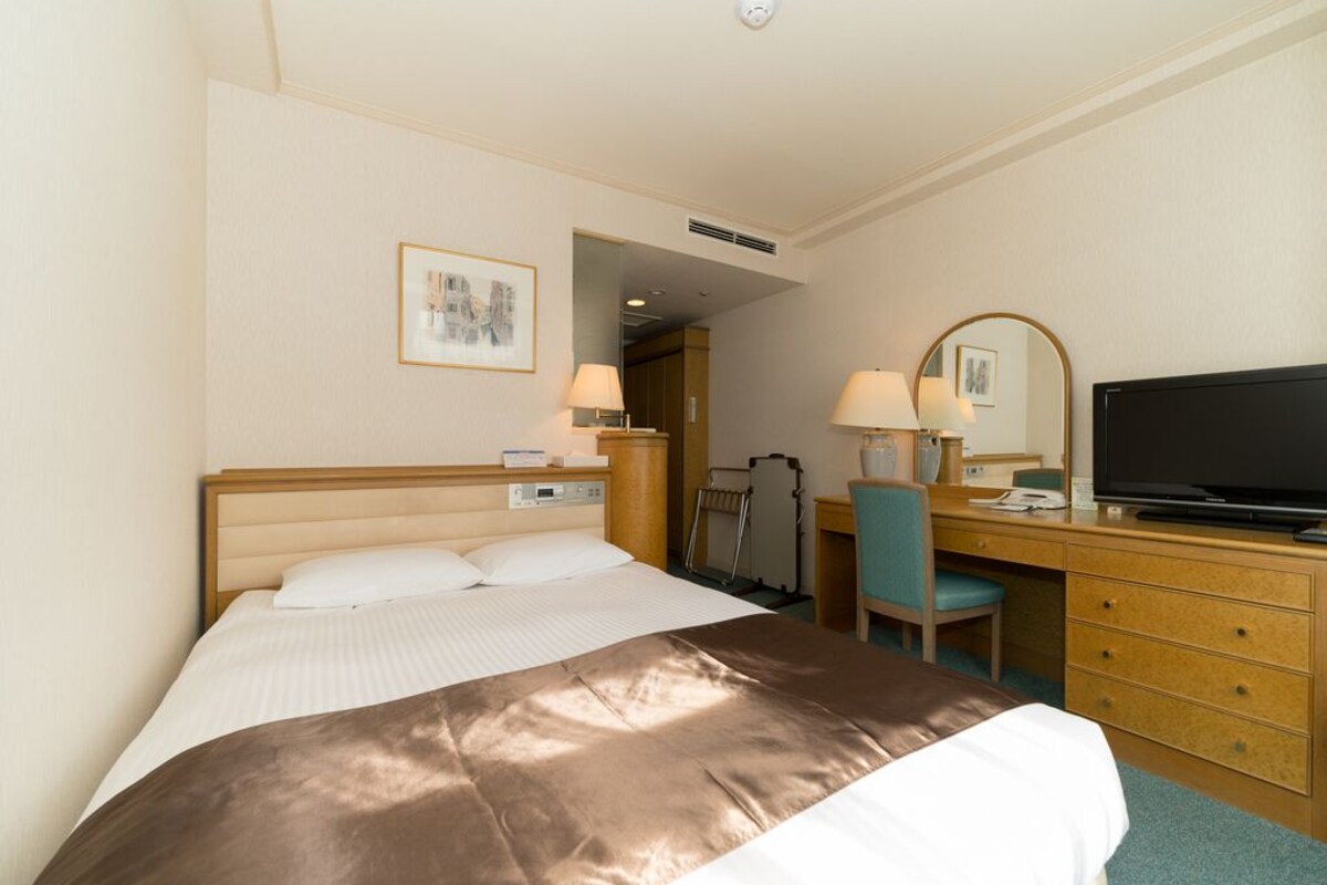 Una camera d'albergo con un letto, una scrivania con una sedia, una televisione e uno specchio.