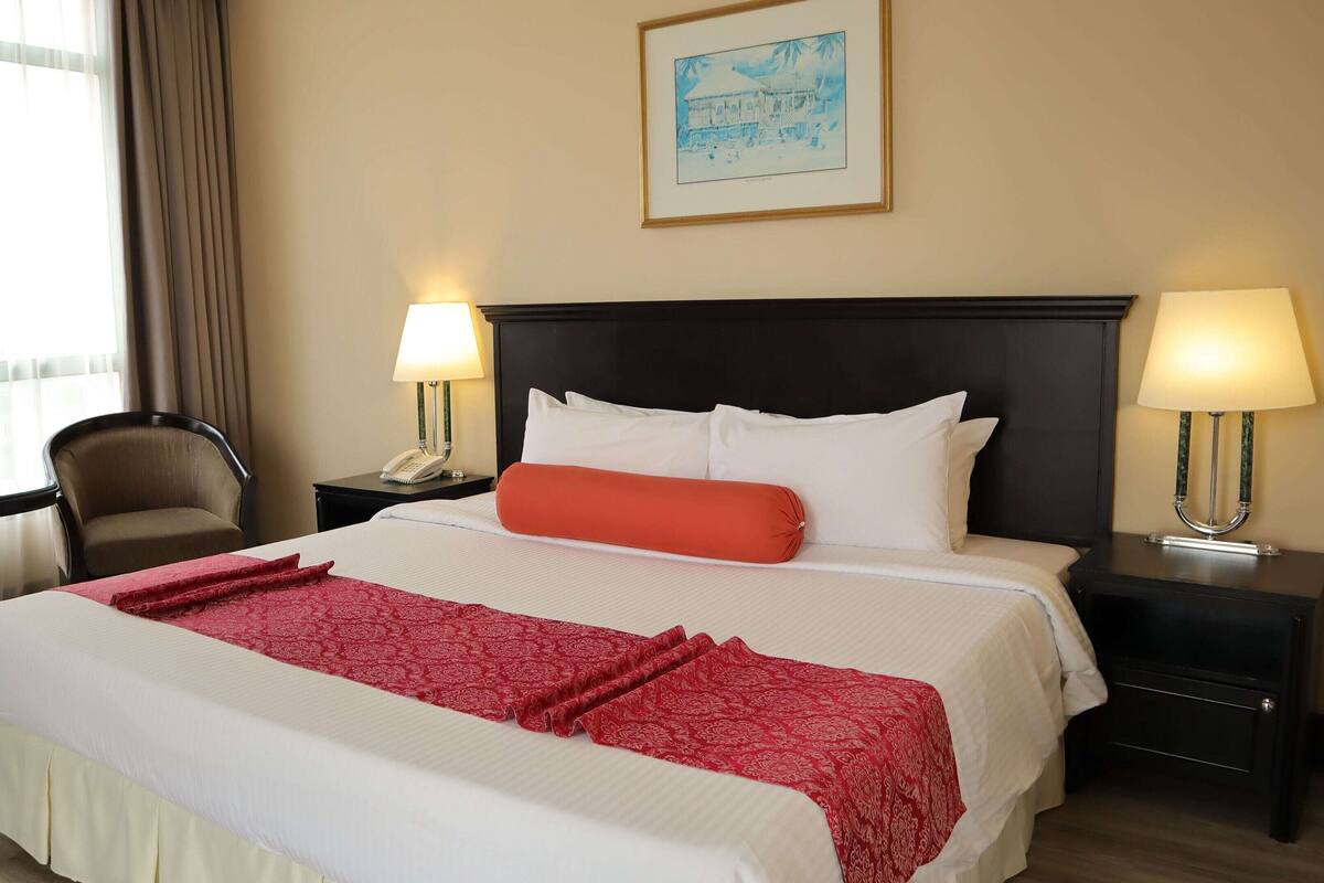 A hotel room with a large bed, two bedside tables with lamps, a chair, and a framed picture on the wall.