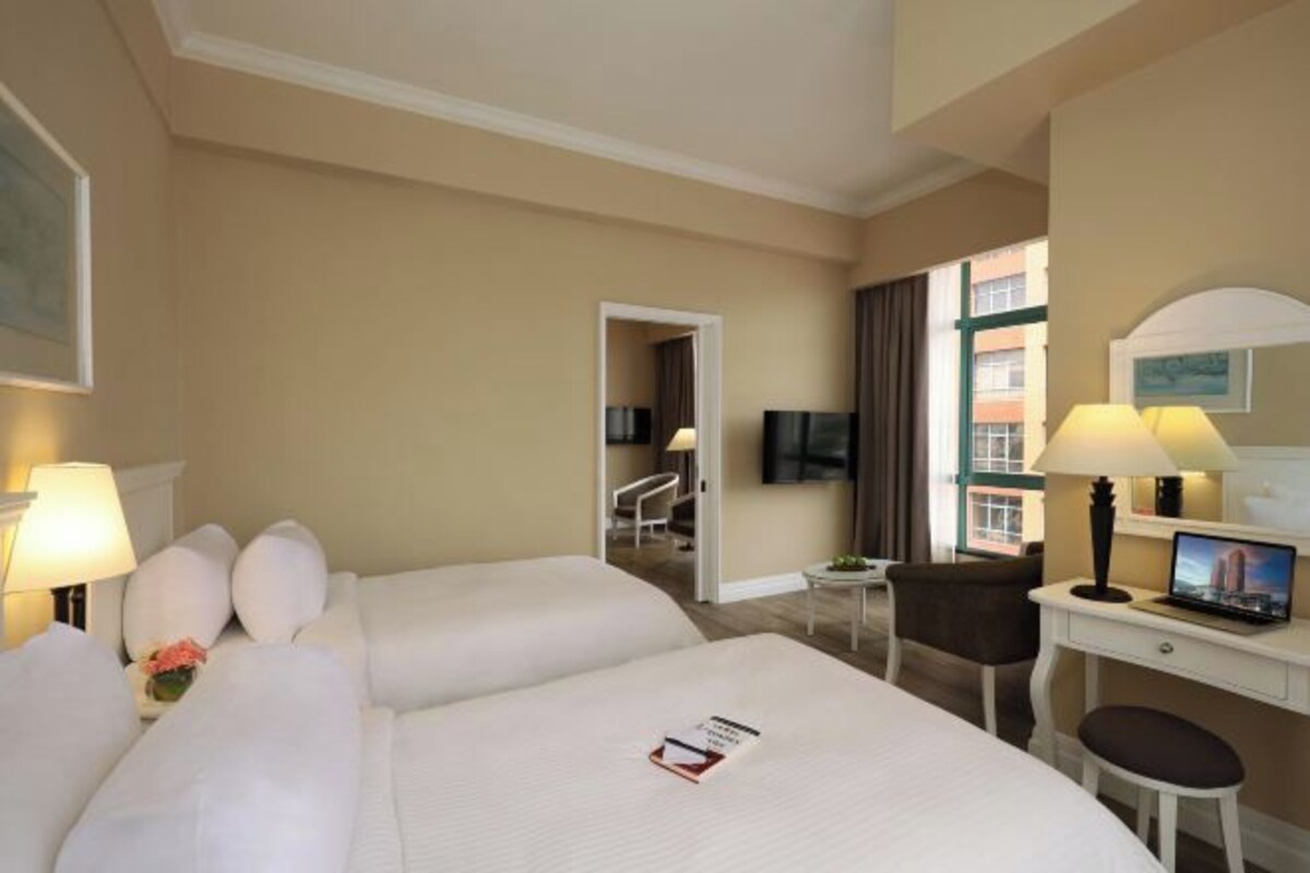 A hotel room with two beds, a desk with a laptop, a chair, and a TV.