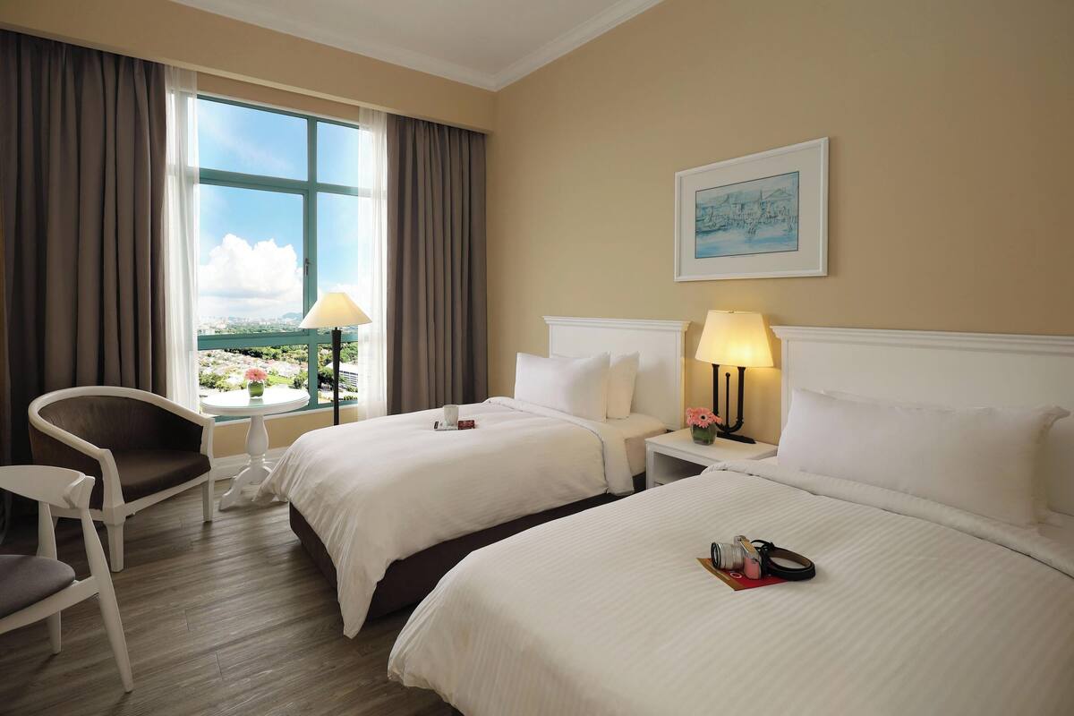 A hotel room with two beds, a chair, a table, and a window with curtains.