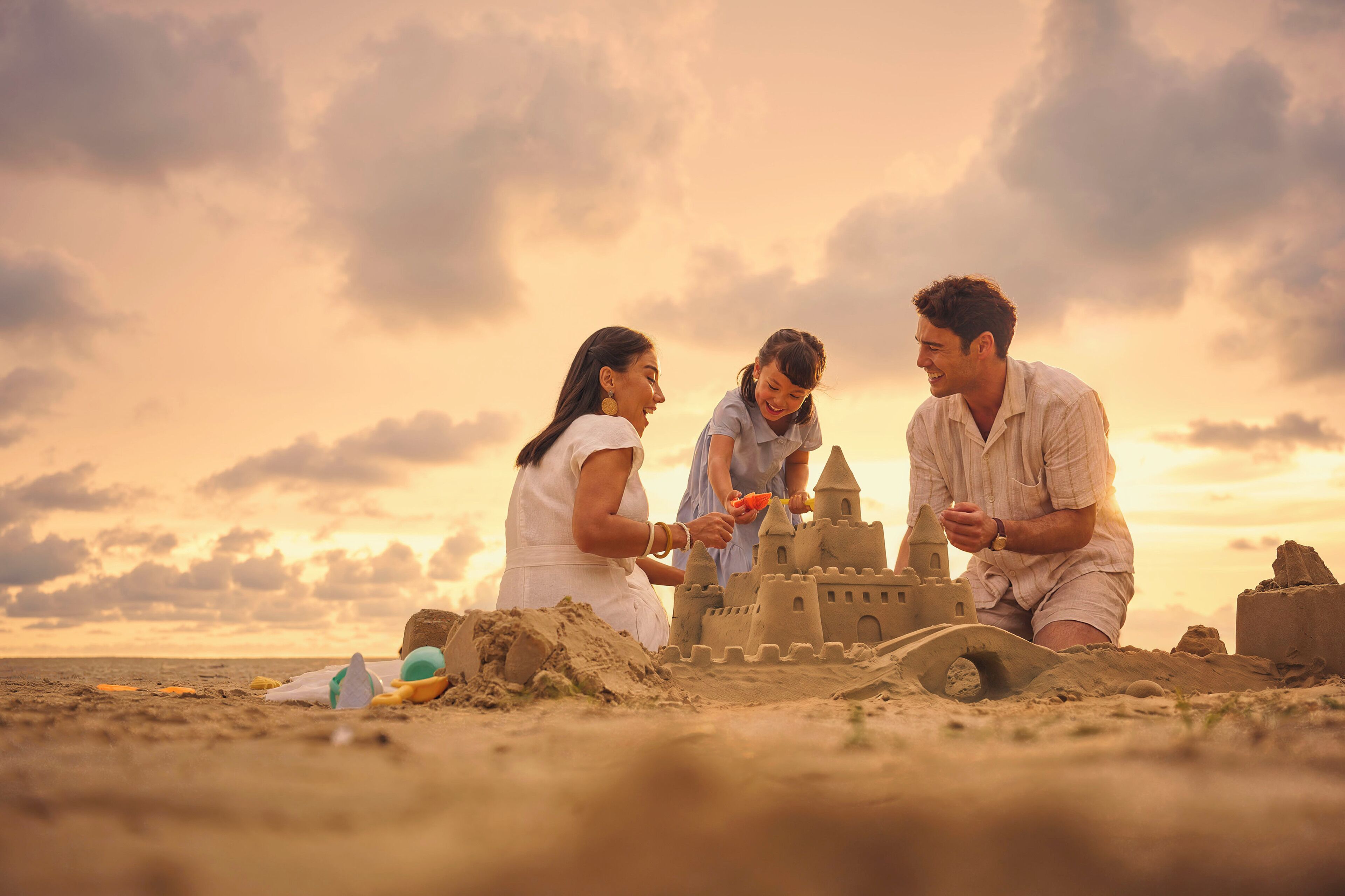 A group of people building a sandcastle on a beach with a sunset in the background.