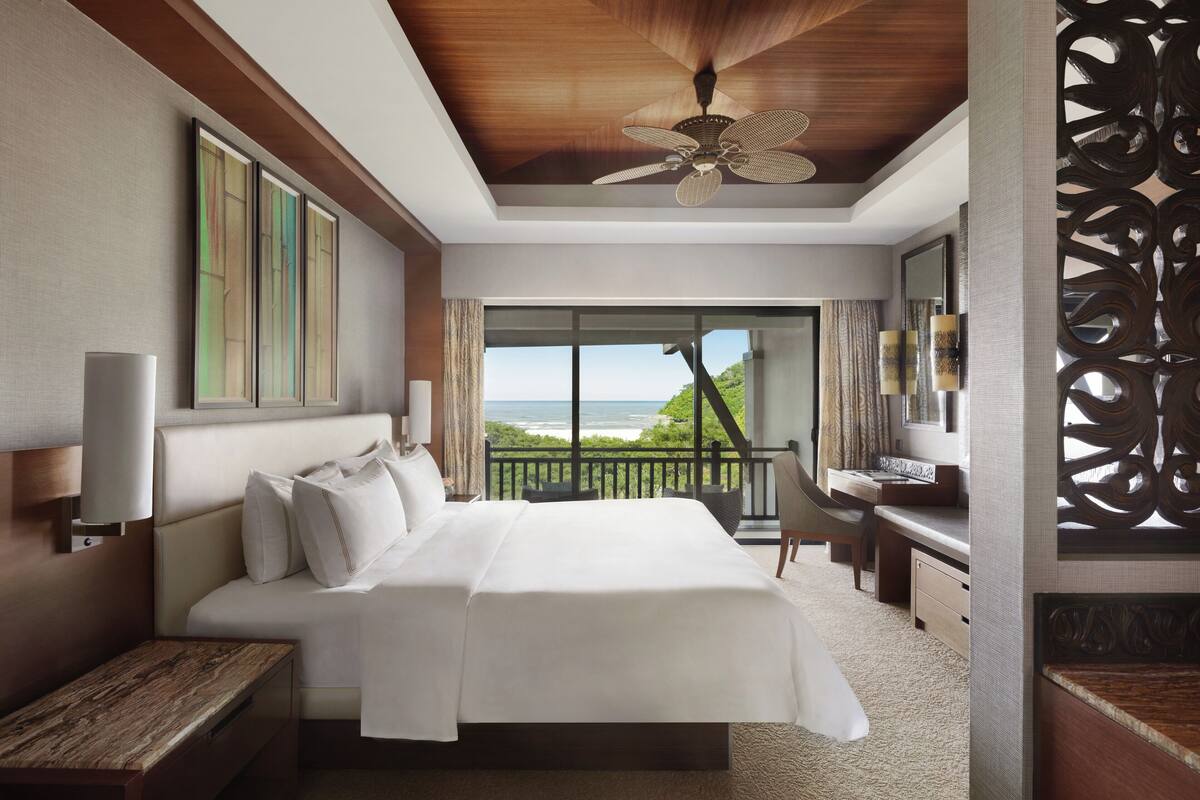 A spacious bedroom with a large bed, a desk, and a view of the ocean.