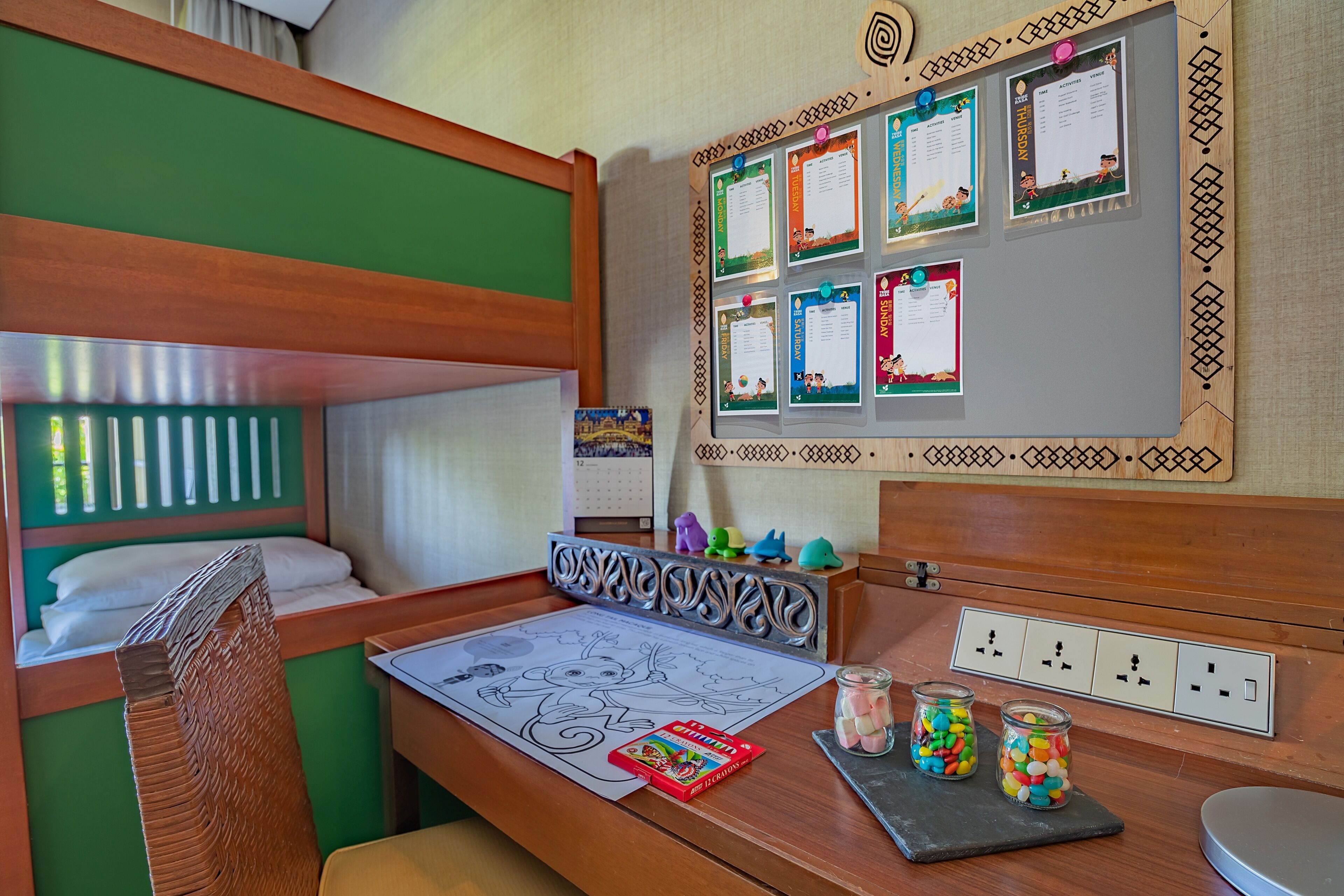 A child's room with bunk beds, a desk with crayons and a calendar, and a wall with activity schedules.