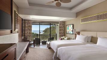 A hotel room with a balcony, a desk, two beds, and a ceiling fan.