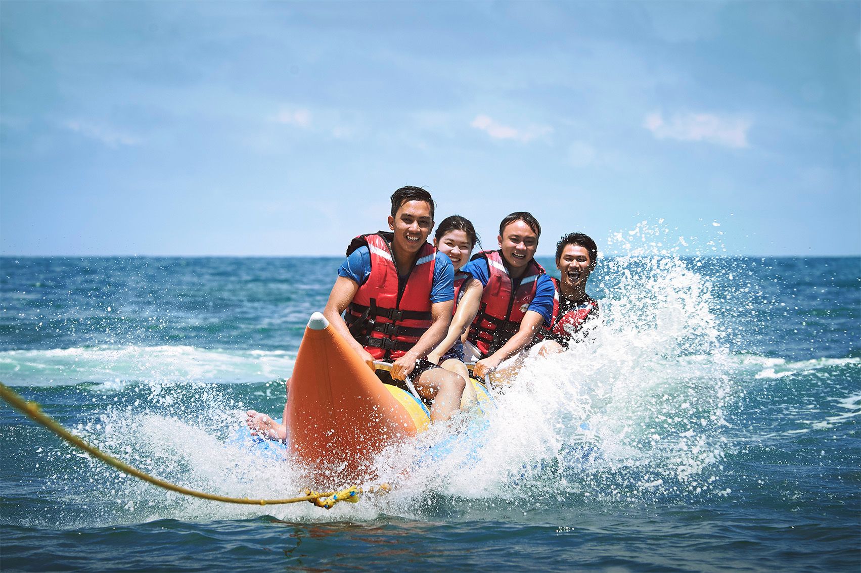A group of people on a watercraft with a rope handle, wearing life jackets.