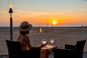 A beach scene with a table and chairs, a fire, and a sunset. - Shangri-La Rasa Ria, Kota Kinabalu (Tuaran)