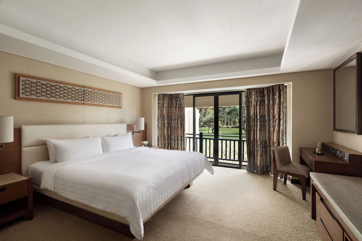 A hotel room with a large bed, a desk, a chair, and a balcony with curtains.