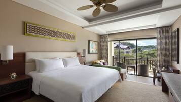 Habitación de hotel con una cama grande, un escritorio, una silla, un balcón con vistas y un ventilador de techo.