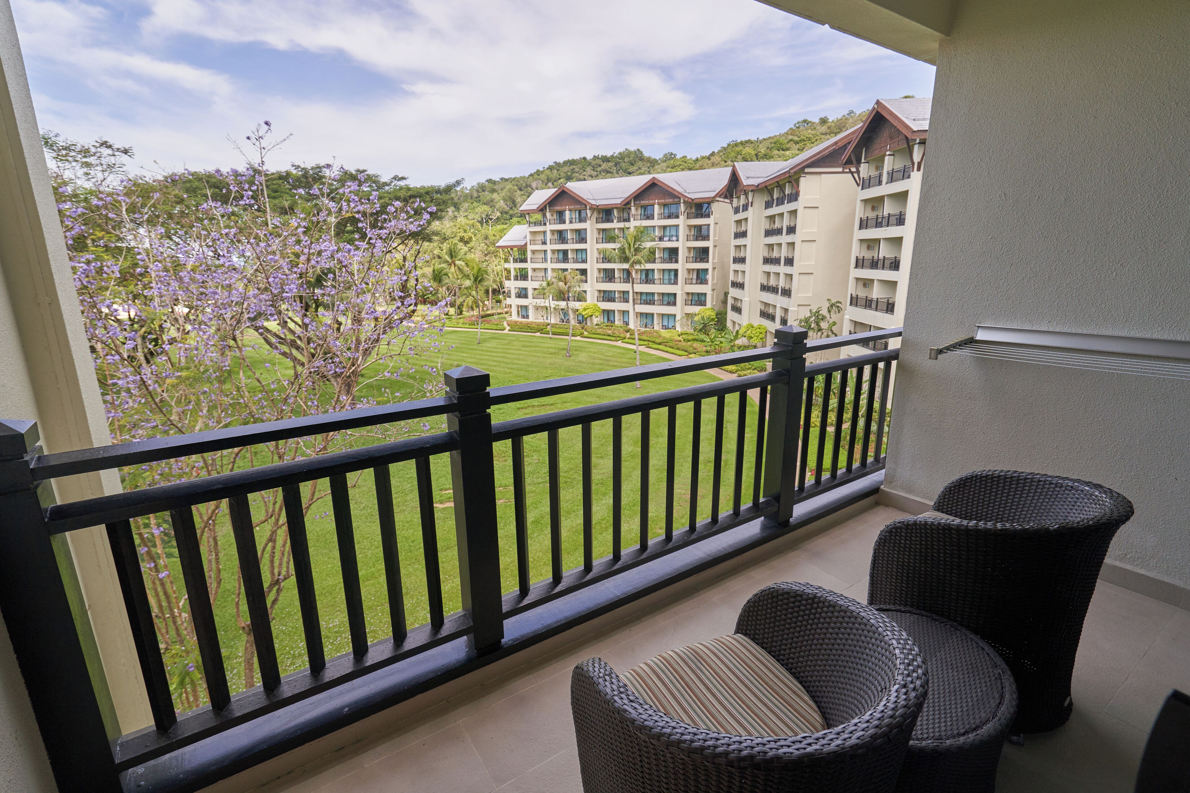 A balcony with wicker furniture, a view of a hotel building, and a well-maintained lawn.