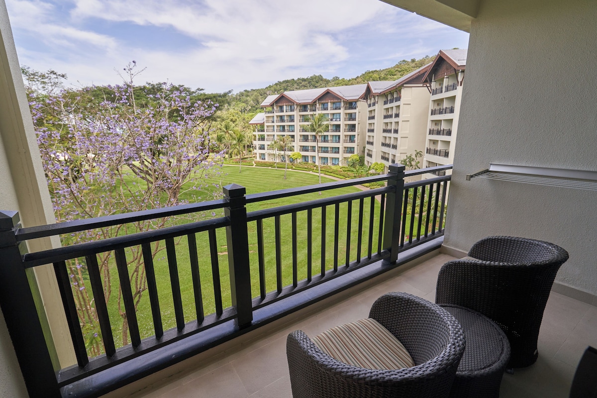 A balcony with wicker furniture, a view of a hotel building, and a well-maintained lawn.