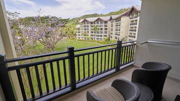 A balcony with wicker furniture, a view of a hotel building, and a well-maintained lawn.