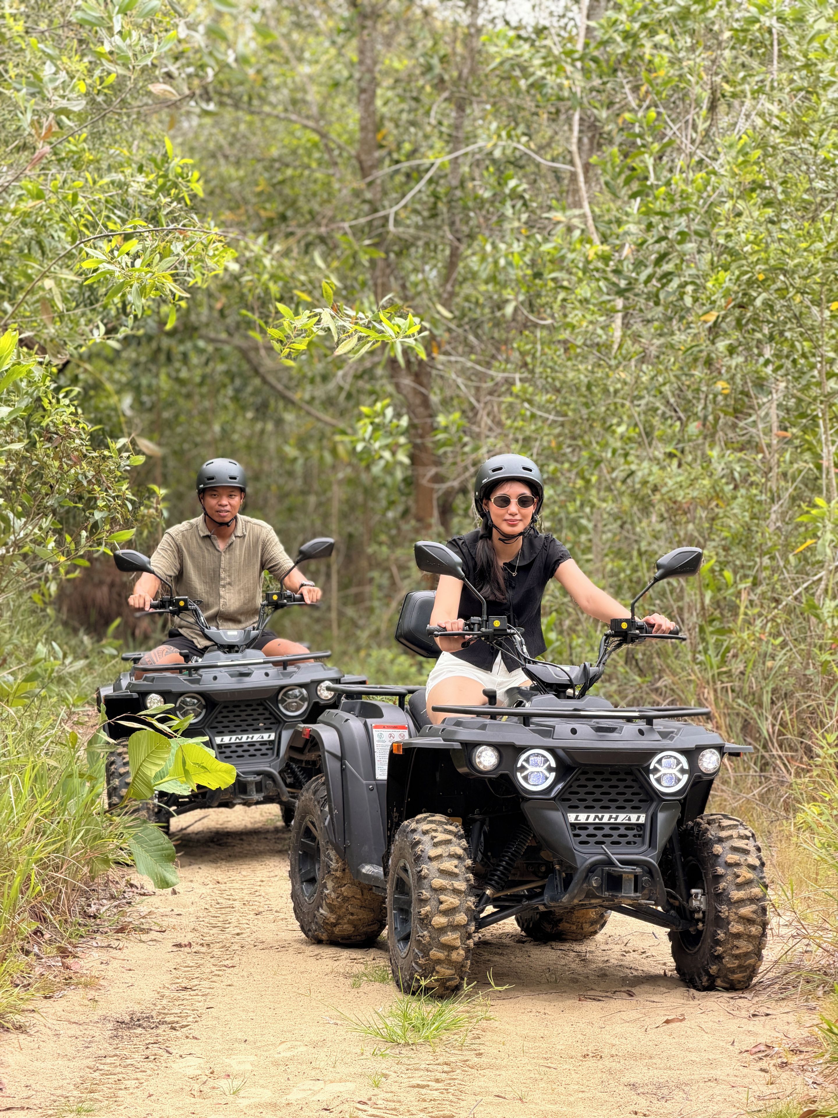 Two people on ATVs on a dirt path surrounded by greenery.