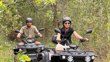 Two people on ATVs on a dirt path surrounded by greenery.