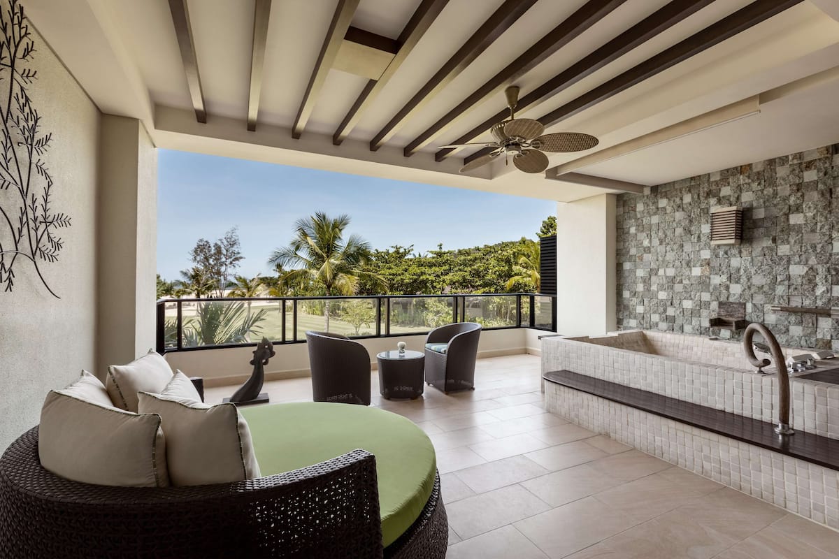 A spacious balcony with a seating area, a jacuzzi, and a view of greenery.