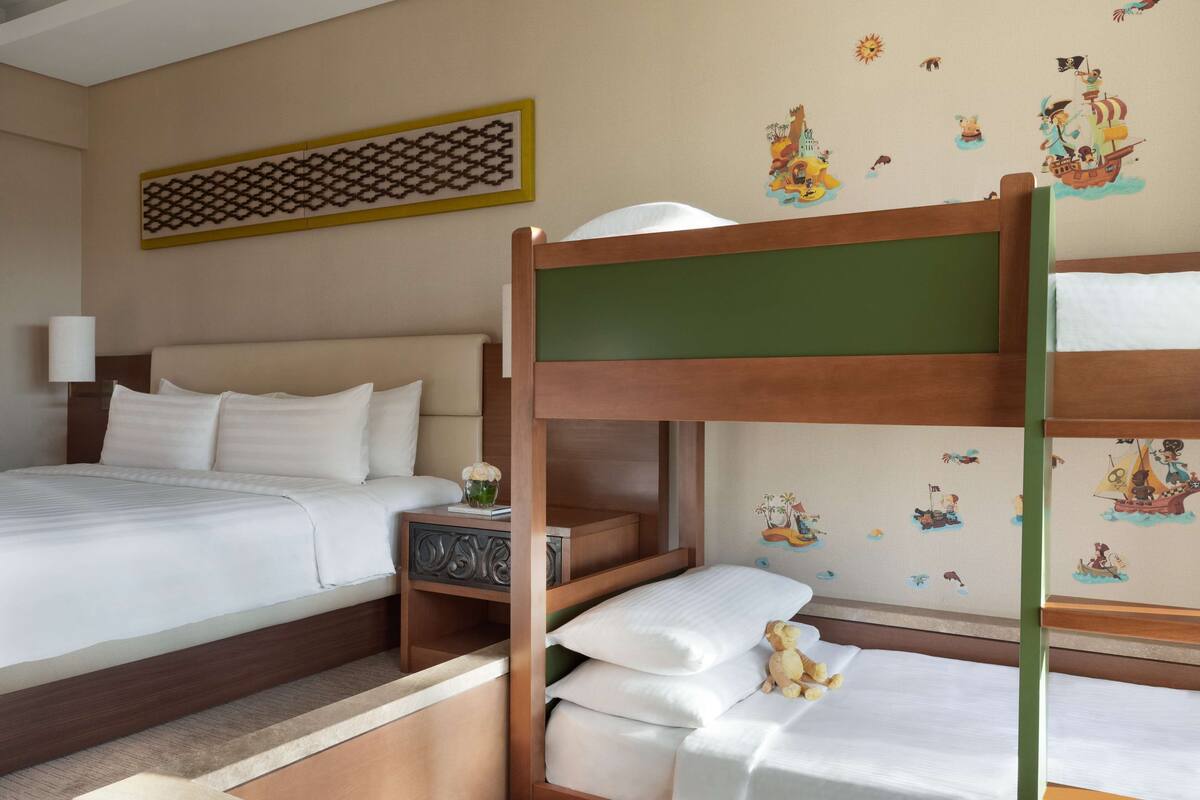 A hotel room with a bunk bed, a single bed, and a nightstand with a lamp.