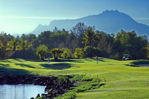 Een golfbaan met een waterpartij, bomen en een berg op de achtergrond.