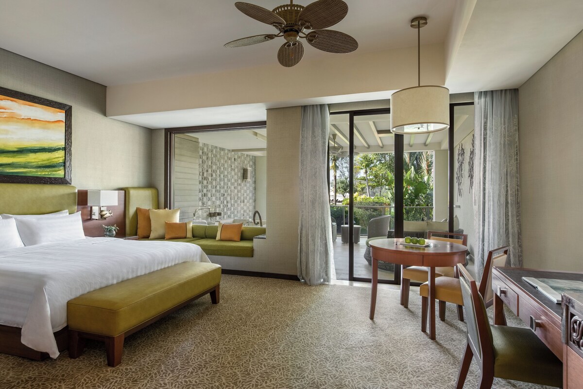 A hotel room with a bed, a desk, a chair, a dining table, and a view of the outdoors.