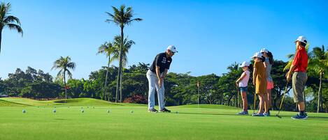 A golf course with a clear sky, palm trees, and a group of people playing golf.