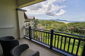 A balcony with wicker chairs and a view of a beach and mountains.