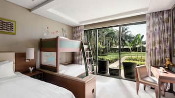 A hotel room with a bunk bed, a desk, a chair, and a view of a garden through a sliding glass door.