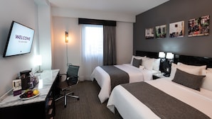 Una habitación de hotel con dos camas, un escritorio con silla, un televisor mostrando 'WELCOME to Laila Hotel', una ventana con cortinas y decoración en la pared.