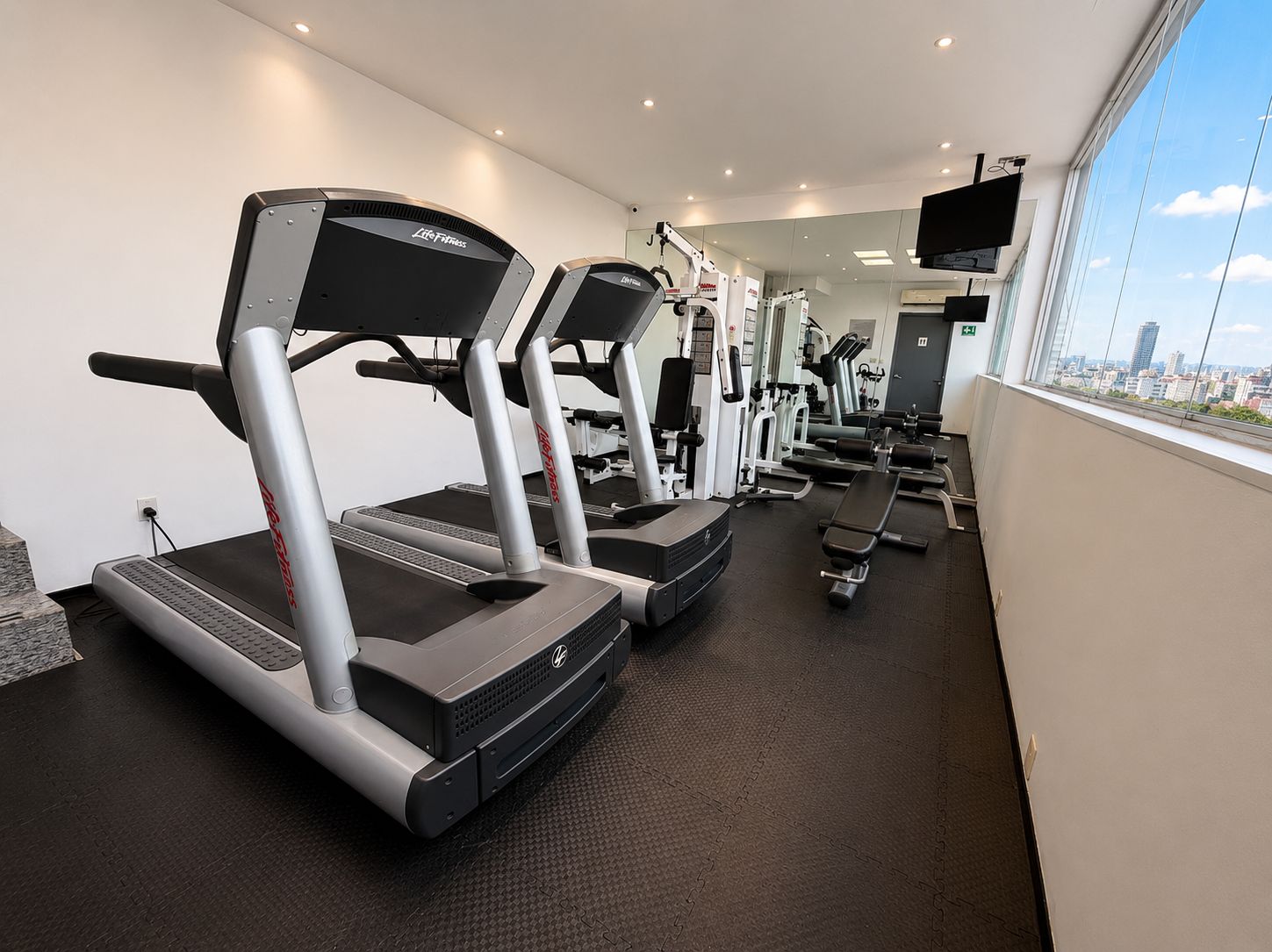 Une salle de sport équipée de tapis de course, d’appareils de musculation et d’un écran de télévision.