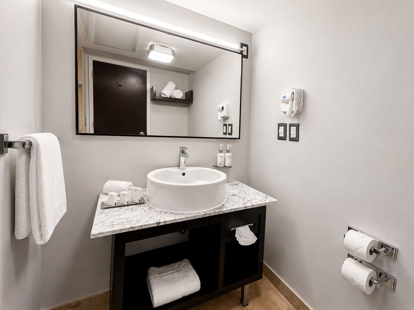 A bathroom with a white sink, a mirror, a towel rack, a towel dispenser, and a toilet paper holder.
