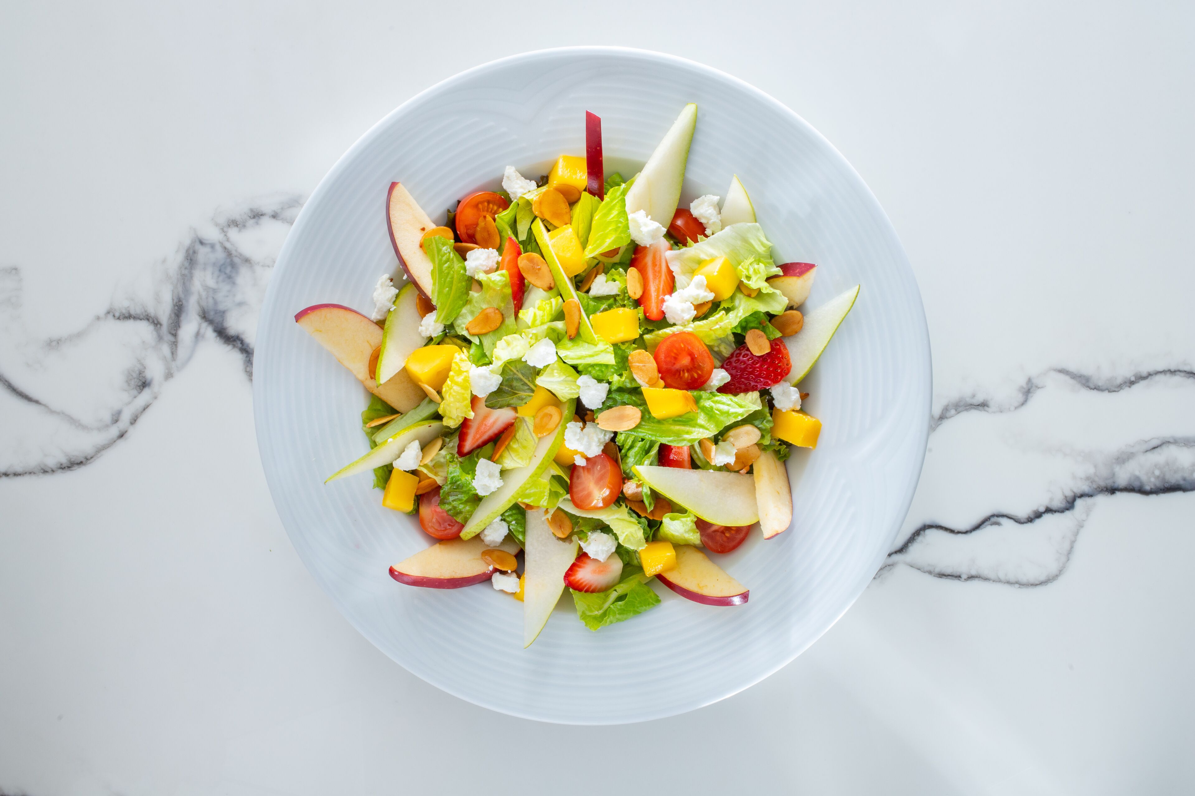 Un tazón de ensalada de frutas sobre una superficie de mármol.