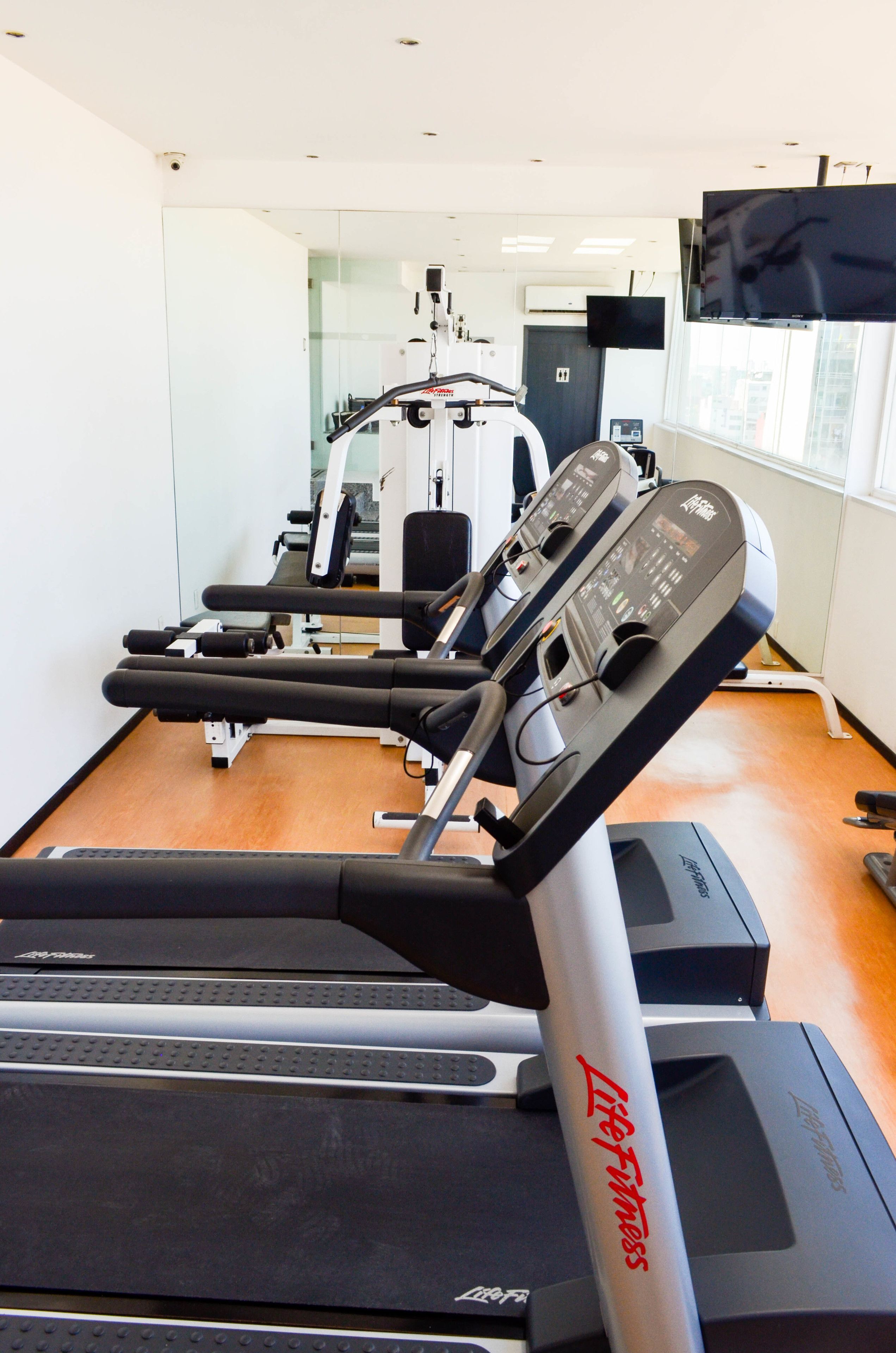 A gym with treadmills, weight machines, and a mirrored wall.