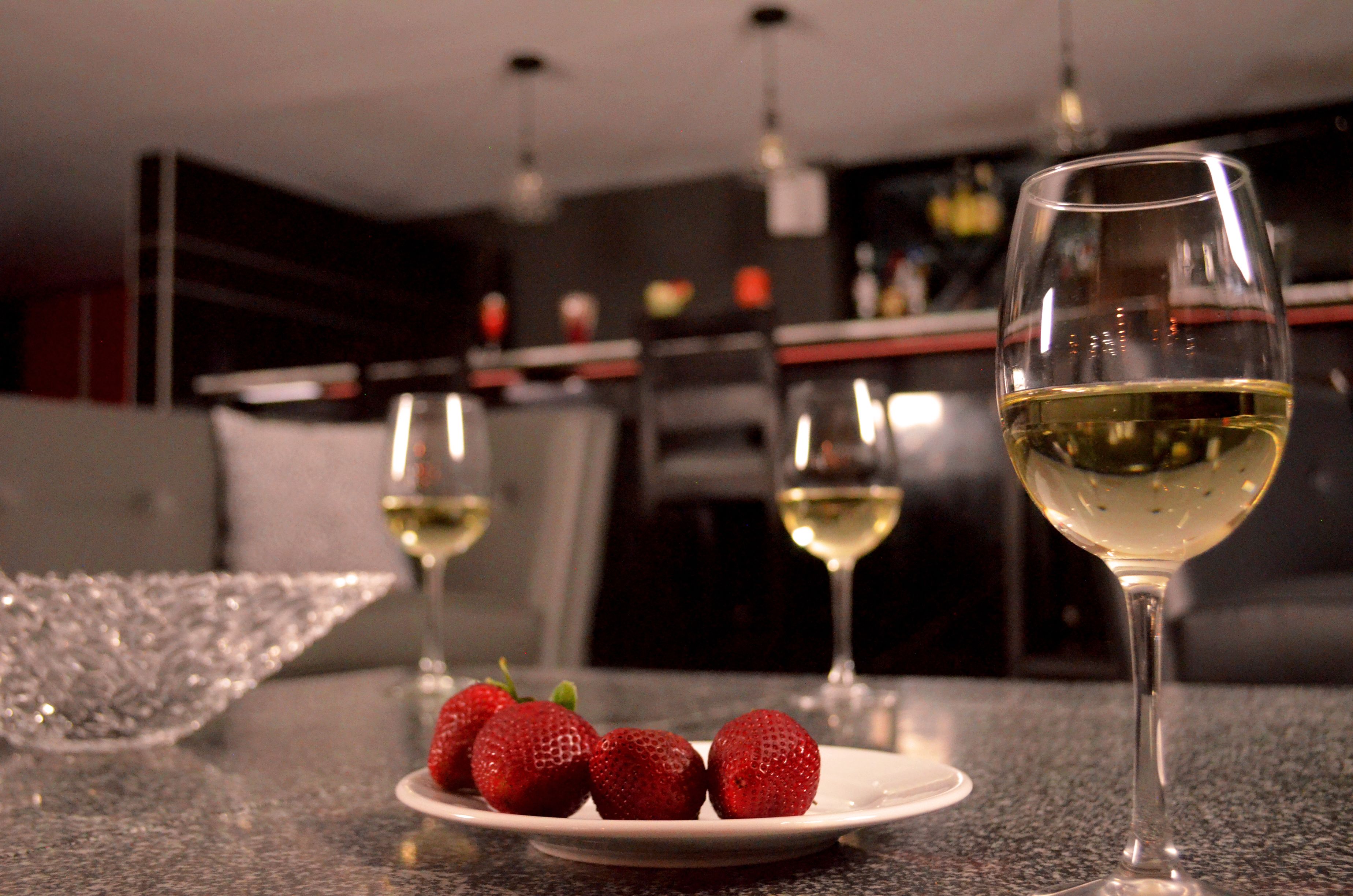 A dining table with a plate of strawberries and two glasses of white wine.