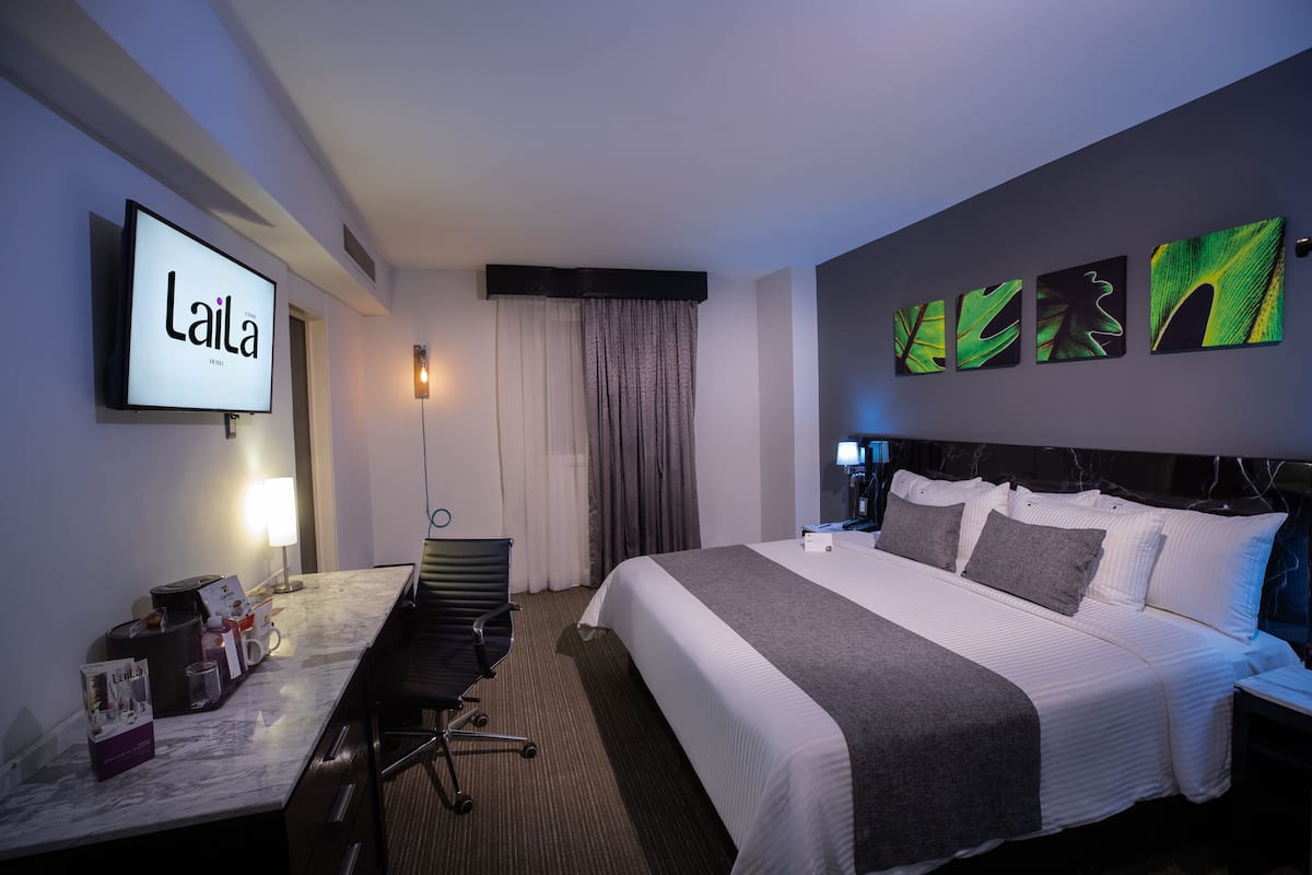 A hotel room with a bed, a desk with a chair, a TV, and artwork on the wall.