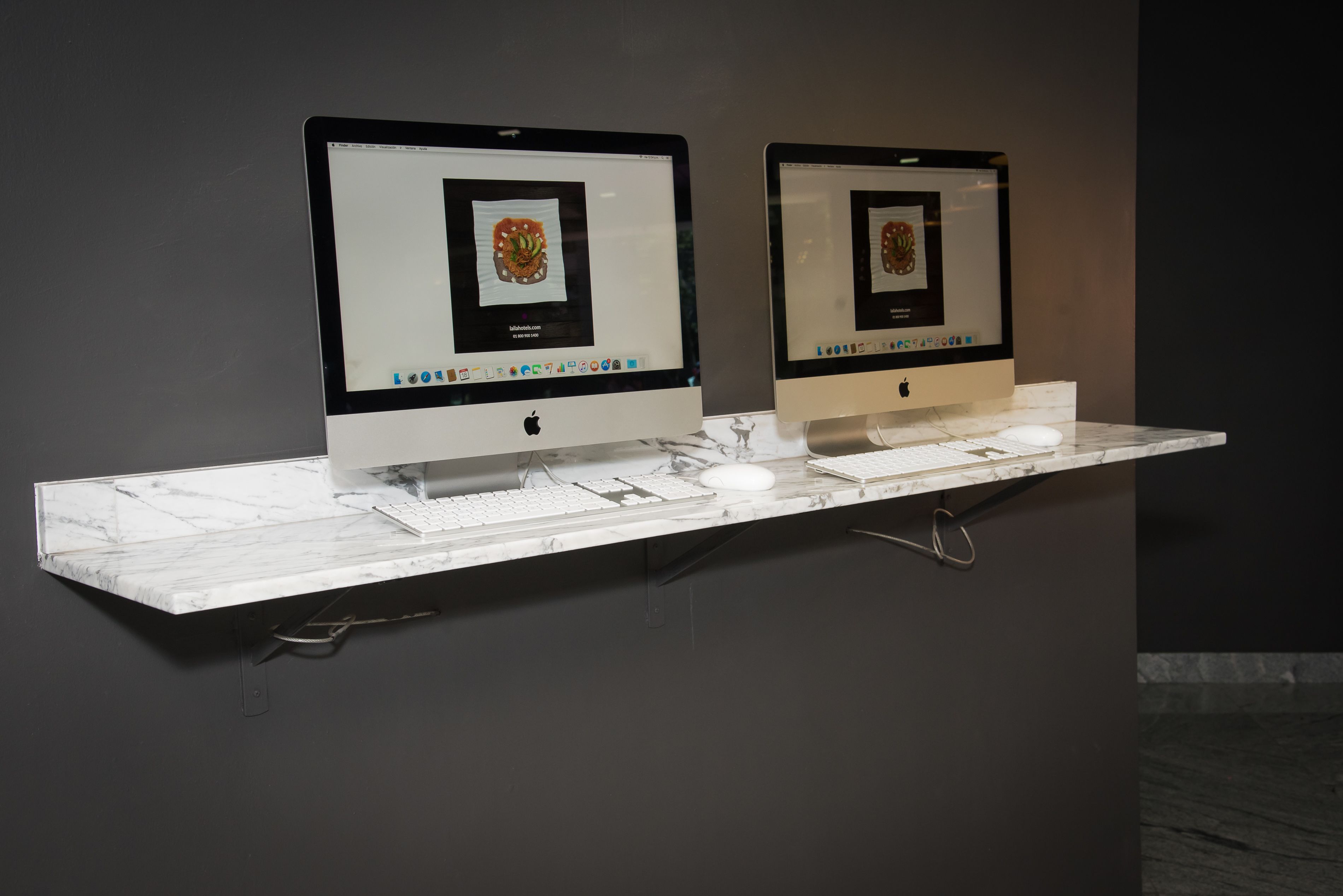 Dos computadoras Apple iMac sobre una encimera de mármol, con un teclado y un ratón.