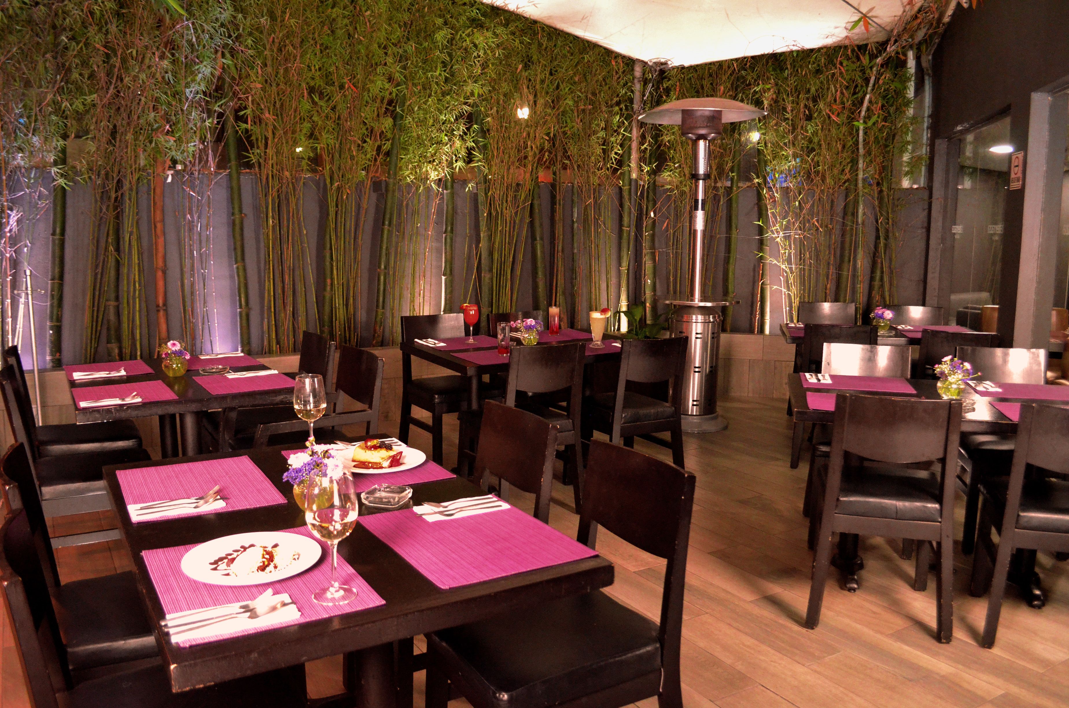 Un restaurante con mesas dispuestas para comer, rodeado de plantas de bambú.